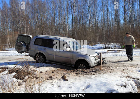 Nazia village, regione di Leningrado, Russia - 17 Marzo 2015: il veicolo è bloccato in un foro in inverno la strada forestale, il driver installare un verricello per il soccorso di t Foto Stock