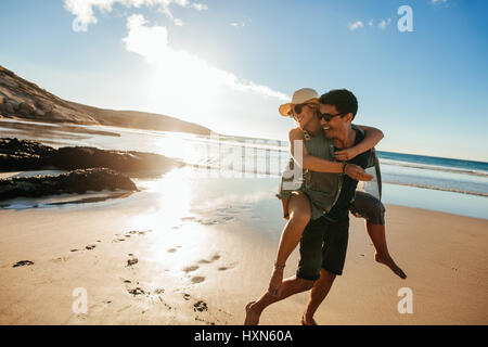 Romantico coppia giovane godendo le vacanze estive. Bel giovane dando piggyback ride alla ragazza sulla spiaggia. Foto Stock