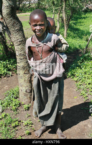 Meserani Snake Park, Arusha, Tanzania - Febbraio 14, 2008: Africa Orientale, sconosciuto Africano nero Maasai ragazzo di 10 anni, è il più giovane sorella dietro Foto Stock