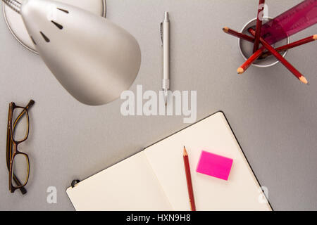 Angolo di alta vista di una raccolta di elementi di scrivania come matite, notebook, lampada, occhiali, penna e gomma in uno stile moderno Foto Stock