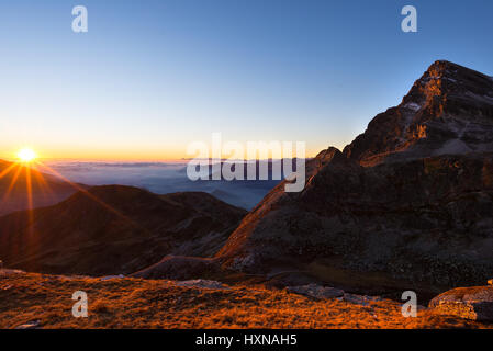 Altitudine elevata gamma di montagna al tramonto con erba incandescente in primo piano. Girato in con retroilluminazione a forma di stella sole delle Alpi italiane. Ampie vie Foto Stock