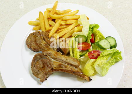 Due costolette di agnello grigliate servita con patatine fritte patatine fritte e insalata di lattuga, pomodori ciliegia e il cetriolo. Foto Stock