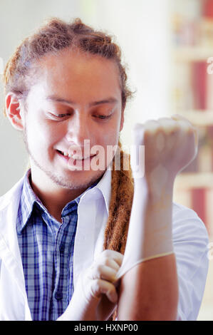 Giovane medico con lunghi dread si blocca in posa per la telecamera mentre mettere dei guanti di gomma, clinica in background, concetto medico Foto Stock