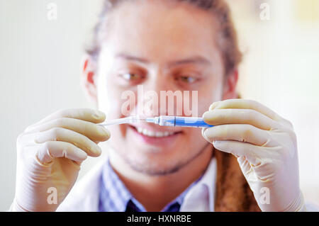 Giovane medico con lunghi dread si blocca in posa per la telecamera tenendo la siringa, clinica in background, concetto medico Foto Stock
