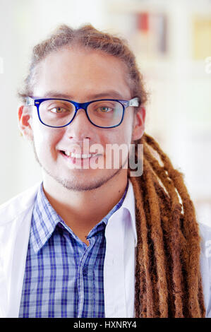 Giovane medico con lunghi dread si blocca in posa per la telecamera mentre sorridente, clinica in background, concetto medico Foto Stock