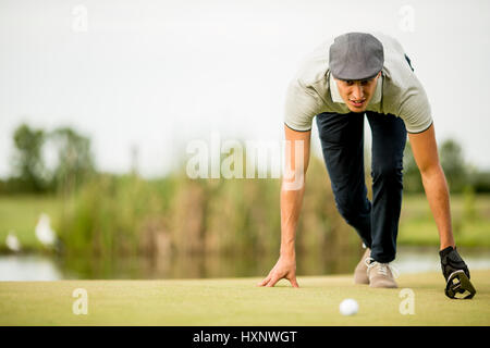 Giovane uomo guardando a sfera mentre accovacciato sul campo da golf Foto Stock