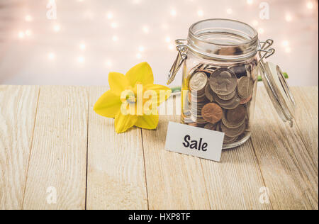 Soldi risparmi jar concetto motivazionale su tavola di legno con giallo daffodil fiore Foto Stock