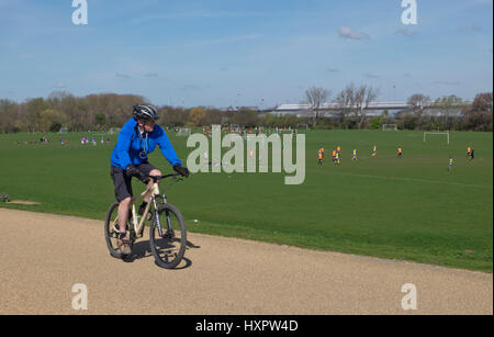 Ciclista va oltre i giocatori a Hackney Marshes calcetto dalla Regina Elisabetta II Londra Olympic Park,UK Foto Stock