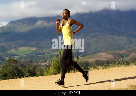 A piena lunghezza lato ritratto di montare la giovane donna africana jogging all'aperto in natura Foto Stock