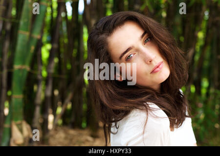 Close up ritratto di attraente giovane donna testa tiltante davanti di alberi di bambù Foto Stock