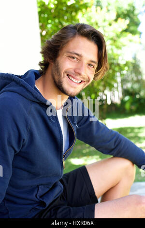 Ritratto di giovane sorridente uomo seduto fuori in estate Foto Stock
