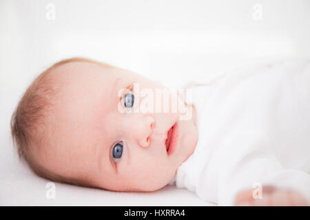 Carino adorabile neonato ragazza nel letto bianco e guardando la telecamera Foto Stock