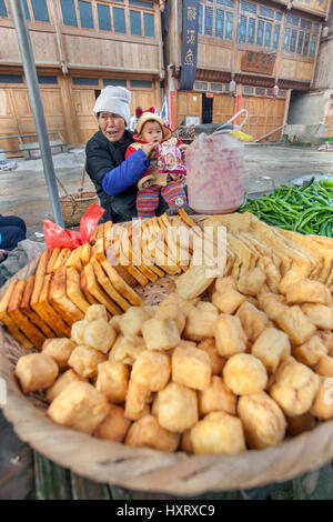 Zhaoxing Dong Village, Guizhou, Cina - 8 Aprile 2010: strada commerciale nella campagna asiatica, una donna anziana tenendo un bambino, vende fritti Foto Stock