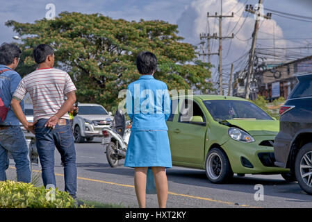 Incidente stradale. I conducenti di sesso maschile e femminile coinvolti in un incidente d'auto si trovano sul lato della strada che osserva il danno. Thailandia Sud-est asiatico Foto Stock