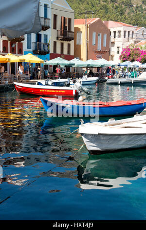 Hafenquai mit bunten Booten, Wasserspiegelung, bunten Häusern, Tischen, Stühlen und Sonnenschirmen, Insel Kastellorizo, Dodekanes, Griechenland Foto Stock