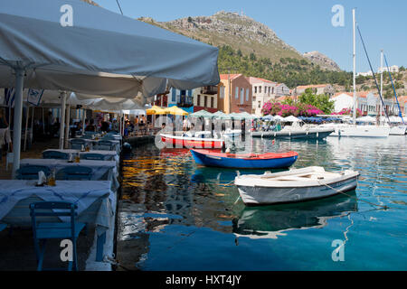 Hafenquai mit bunten Booten, Wasserspiegelung, bunten Häusern, Tischen, Stühlen und Sonnenschirmen, Insel Kastellorizo, Dodekanes, Griechenland Foto Stock