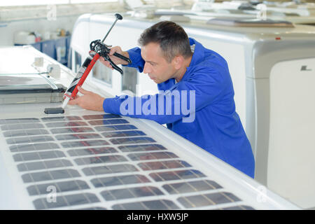 Montatore applicando sillicone intorno al pannello solare Foto Stock