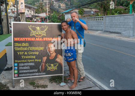 Kru Sak, il Muay Thai o Thai boxer, pone accanto a un cartellone presenta la sua palestra mentre un turista occidentale si unisce a Phuket , della Thailandia. 09-Mar-2017 Foto Stock