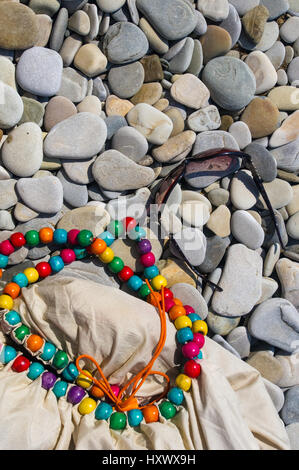 Borsa da spiaggia e occhiali da sole sulla spiaggia di ciottoli, tramonto Foto Stock