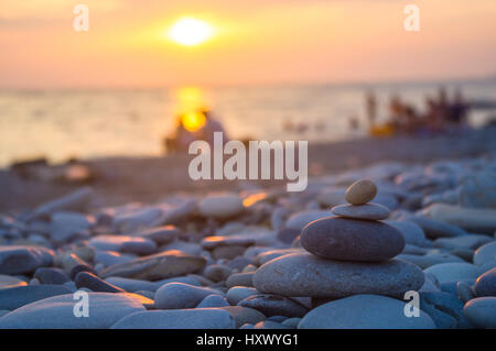 Un giovane e ripiegati a piramide Zen pietre ghiaia sul mare spiaggia al tramonto Foto Stock