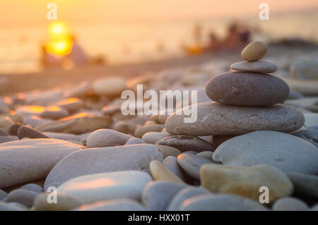 Un giovane e ripiegati a piramide Zen pietre ghiaia sul mare spiaggia al tramonto Foto Stock