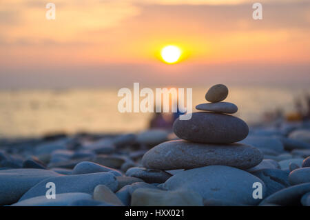 Un giovane e ripiegati a piramide Zen pietre ghiaia sul mare spiaggia al tramonto Foto Stock