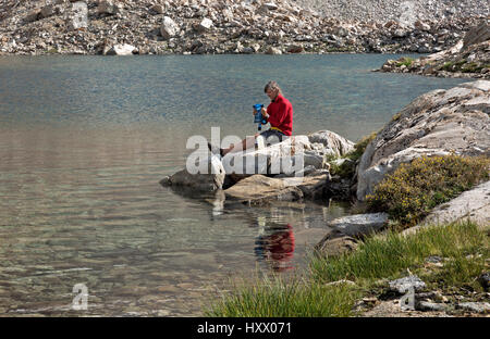 CA03142-00...CALIFORNIA - John Muir Trail escursionista utilizzando un sacchetto di squeeze per purificare l acqua a una piccola tarn sopra il lago di Marjorie in Kings Canyon National Park. Foto Stock