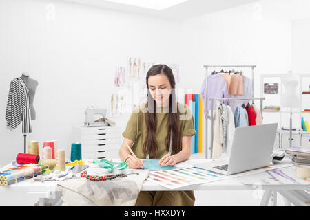 Una giovane designer di moda disegno presso il desk nel suo showroom Foto Stock