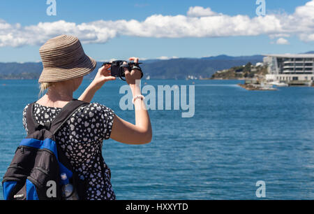 Wellington, Nuova Zelanda - 11 Febbraio 2017: una donna con un cappello e uno zaino, è scattare una foto con una Nikon fotocamera compatta al waterfront di Welli Foto Stock