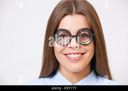 Ritratto in studio di divertenti happy young business woman in big nerd occhiali su sfondo grigio. Foto Stock