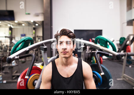 Montare giovane uomo ispanico nella palestra di andare a lavorare sulla macchina fitness, flex muscoli. Allestitore preparato per la formazione, andando a fare shoulder press. Foto Stock
