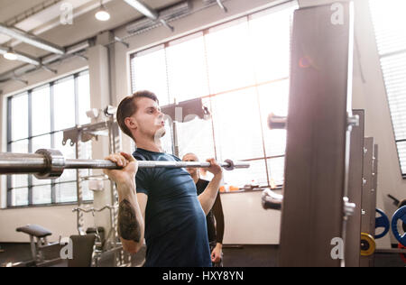 Giovane bello montare l'uomo in palestra con il suo personal trainer lavora fuori, barra di sollevamento del barbell, muscoli di flessione Foto Stock