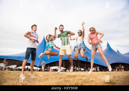 Un gruppo di ragazzi adolescenti e ragazze presso i festival estivi di musica, balli e i salti nella parte anteriore della tenda grande, giornata di sole Foto Stock