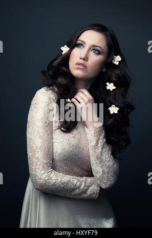 Donna che indossa un bianco Abito in pizzo è alla ricerca di distanza, ha fiori nei suoi capelli Foto Stock