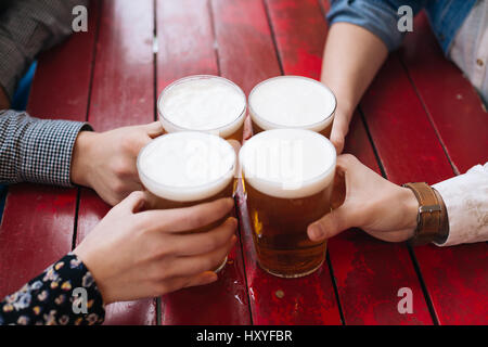 Quattro persone mani bevendo una birra su di un rosso tavolo in legno Foto Stock