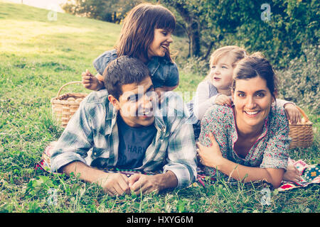 La famiglia felice di quattro giacente in erba in autunno dopo la raccolta di mele. Effetto caldo aggiunto. Foto Stock