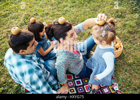 Famiglia sdraiati sull'erba a giocare con le mele sulla testa dopo il prelievo Foto Stock