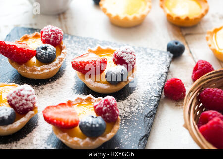 La preparazione di piccole tortine di pasta riempita con vainila panna e frutti di bosco freschi in un bianco rustico tavolo in legno Foto Stock