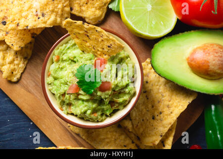 Guacamole ciotola con ingredienti e tortilla chips su un tagliere di legno. Vista superiore Foto Stock