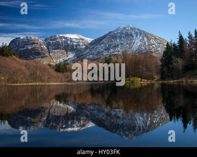 Montagne innevate si riflette in una loch in Glencoe, Scozia in Primavera Foto Stock