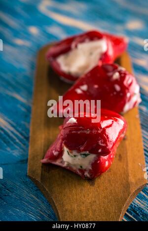 Foto verticale di tre red hot chili peppers che sono disposti in una fila sul piatto di legno cucchiaio. Vegetale è riempito da formaggio fresco con erbe aromatiche. Tutto è p Foto Stock