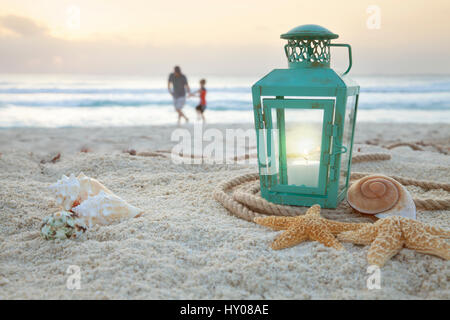 Lanterna con conchiglie sulla spiaggia con soft focus padre e figlio raccogli conchiglie in background di sunrise Foto Stock