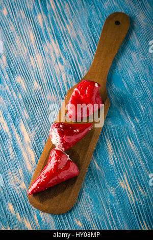 Foto verticale di tre red hot chili peppers che sono disposti in una fila sul piatto di legno cucchiaio. Vegetale è riempito da formaggio fresco con erbe aromatiche. Tutto è p Foto Stock