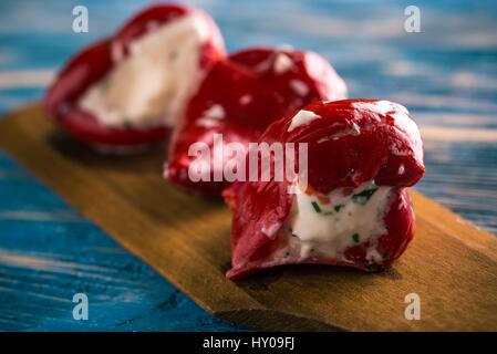 Foto orizzontale di tre red hot chili peppers che sono disposti in una fila sul piatto di legno cucchiaio. Vegetale è riempito da formaggio fresco con erbe aromatiche. Tutti è Foto Stock