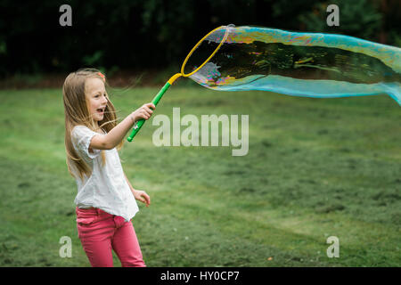 Giovani Bond Girl soffiando una bolla di sapone gigante nel Parco Foto Stock