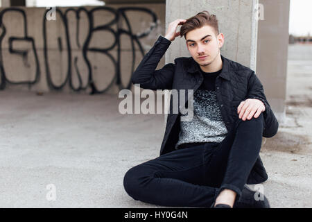 Moda uomo seduto vicino al muro con gli occhiali sulle mani Foto Stock