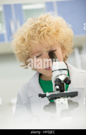 Little Boy in camice guardando attraverso il microscopio Foto Stock