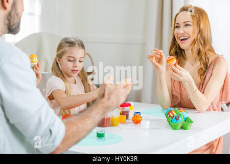 Felice famiglia giovane seduta a tavola e pittura delle uova di Pasqua insieme Foto Stock