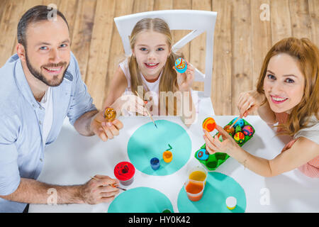 Vista superiore della famiglia felice al tavolo di pittura delle uova di Pasqua insieme Foto Stock