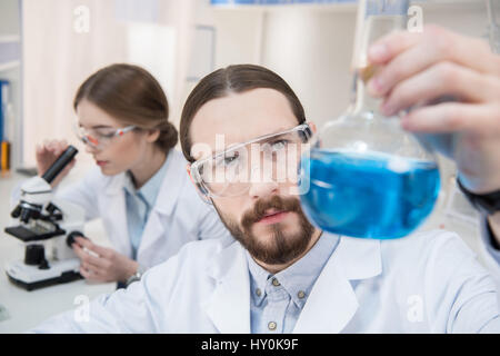 Malinconici scienziato maschio holding pallone con reagente chimico Foto Stock